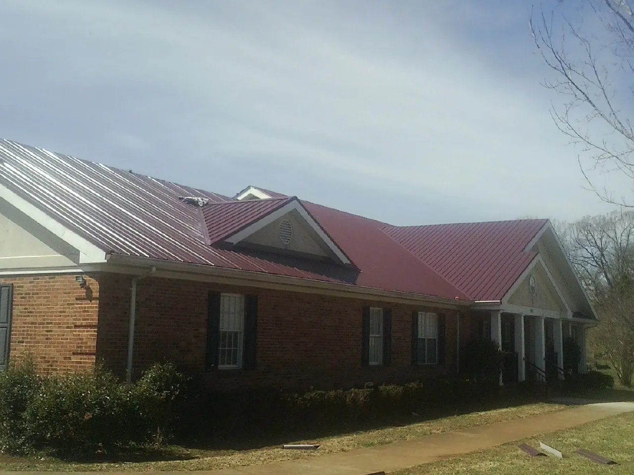 Red metal roof with gabled entries on a long brick building, from a Hail Damage Roof Repair job in Venice