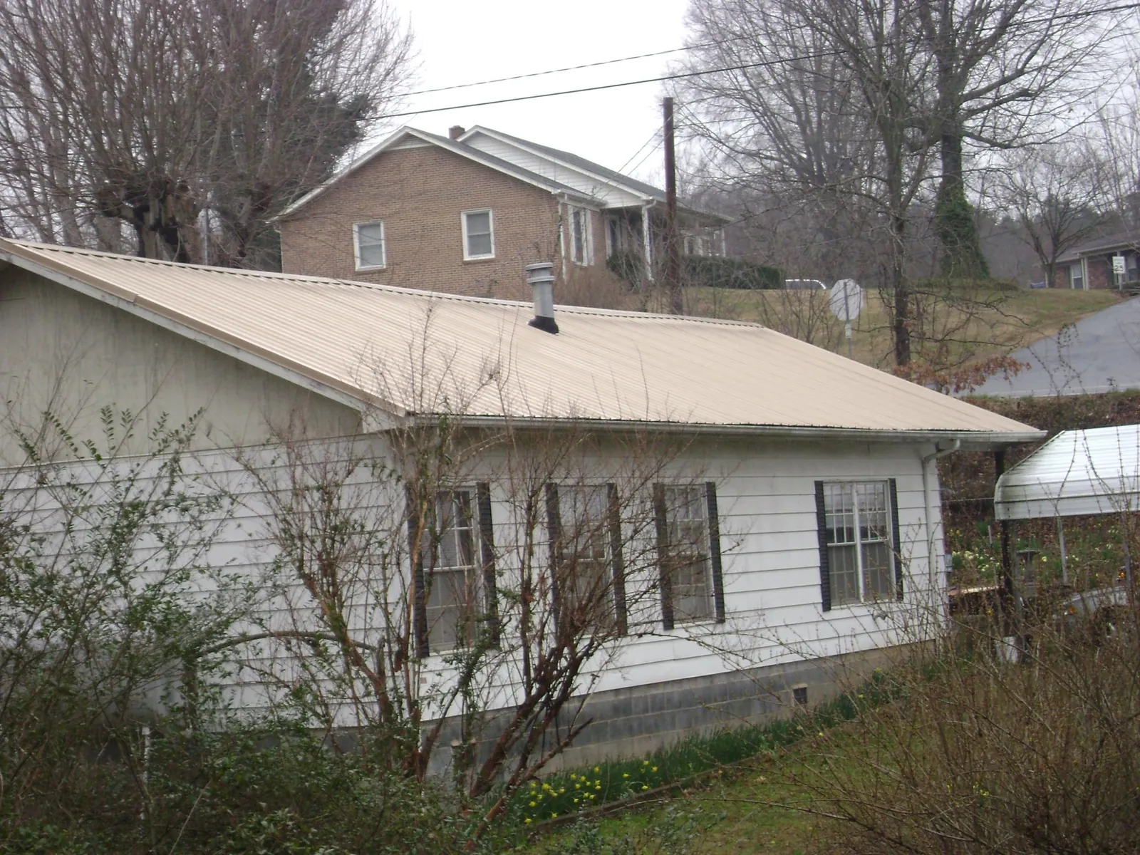 Tan metal roof on a white sided house set into a hillside — Commercial Roofing by Roofing Brothers in Venice